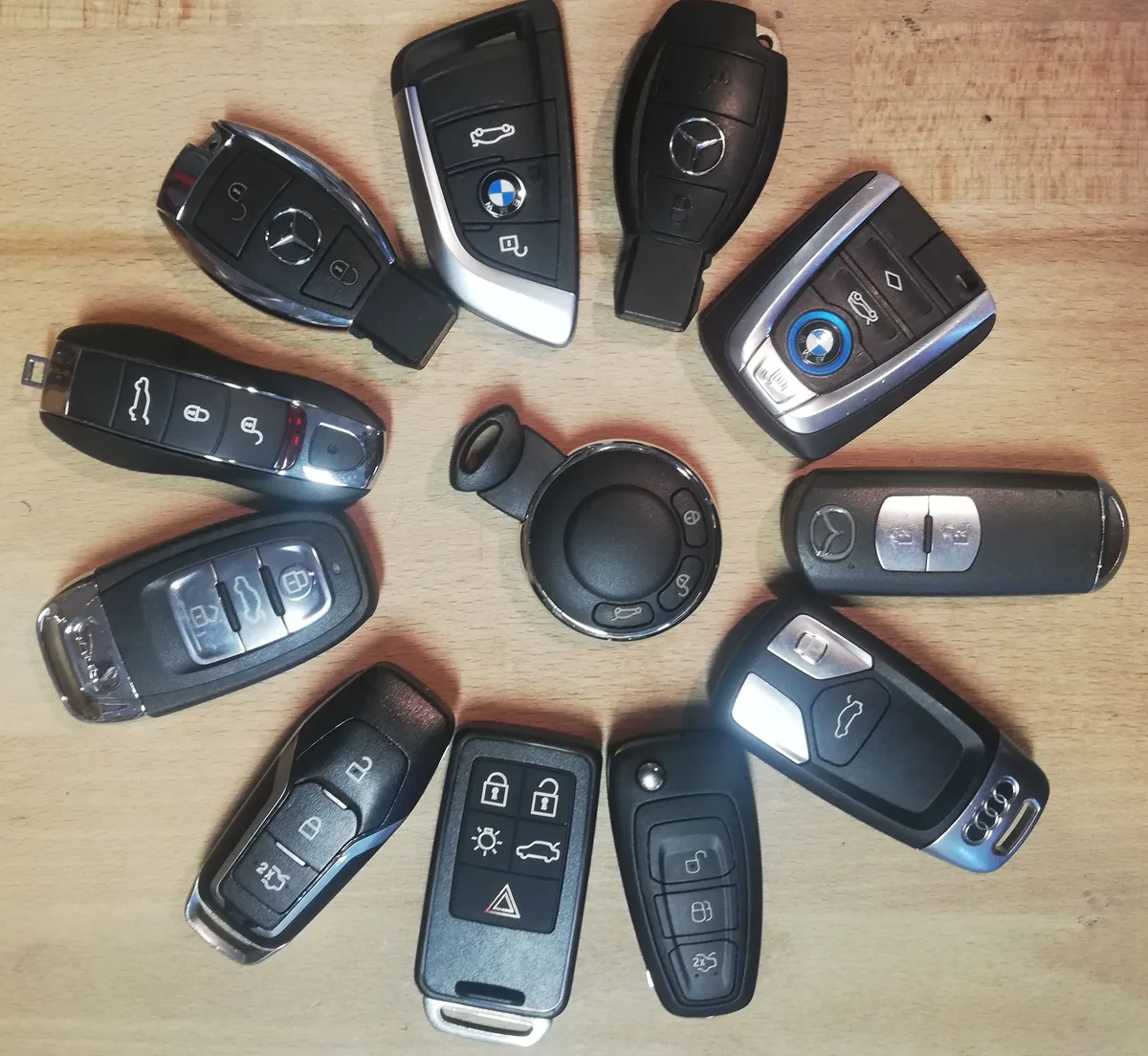 Funkschlüssel verschiedener Automarken – BMW, Mercedes, Audi, Ford, Volvo und weitere – auf einem Holztisch angeordnet